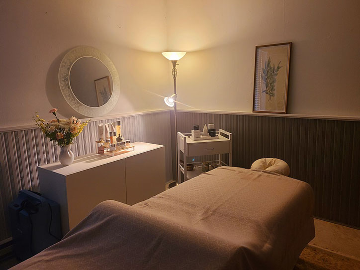A serene massage room featuring a white treatment bed and a large mirror reflecting the calming atmosphere.