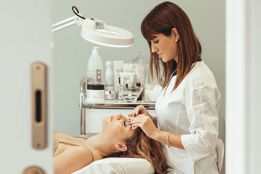 A woman receiving eyebrow shaping from a doctor in a clinical setting.
